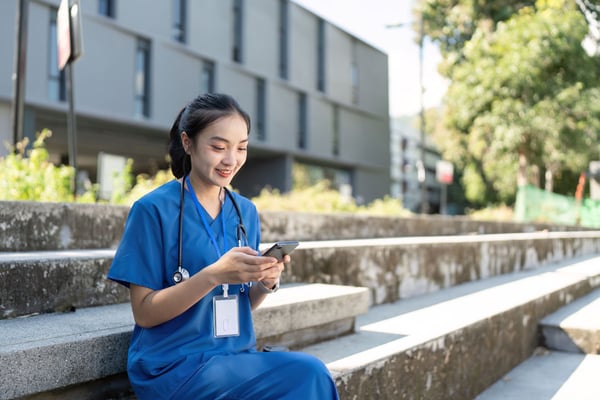 smiling-female-doctor-in-blue-scrubs-outdoors-on-mobile-device