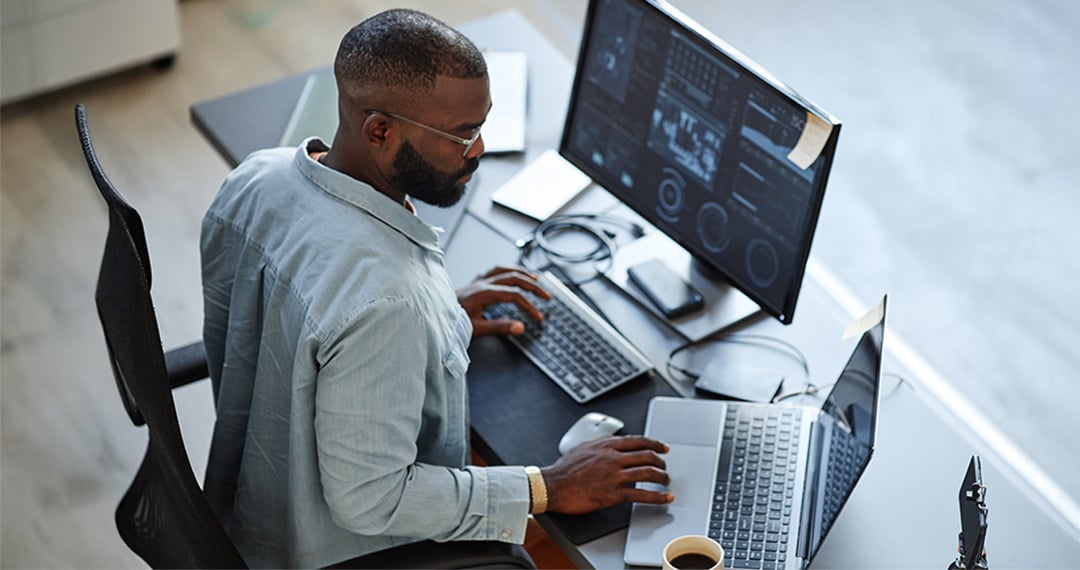 man-working-from-laptop-and-desktop-computer
