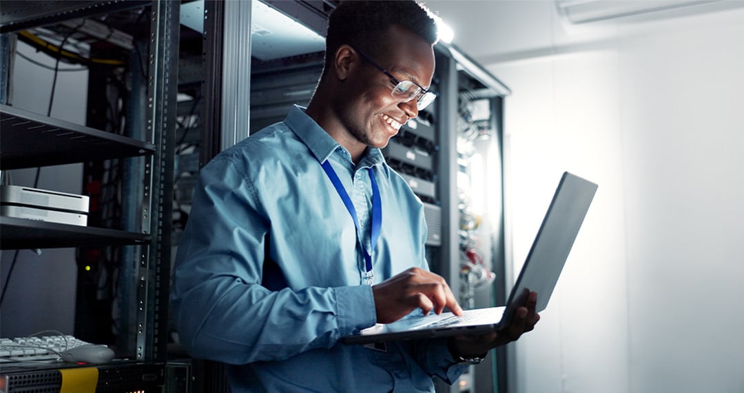 smiling-IT-tech-on-laptop-in-data-center