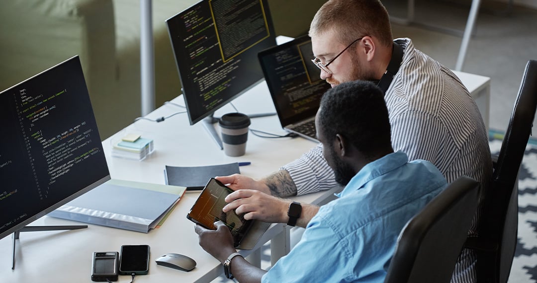 two-men-at-workstations-reading-data-on-mobile-device